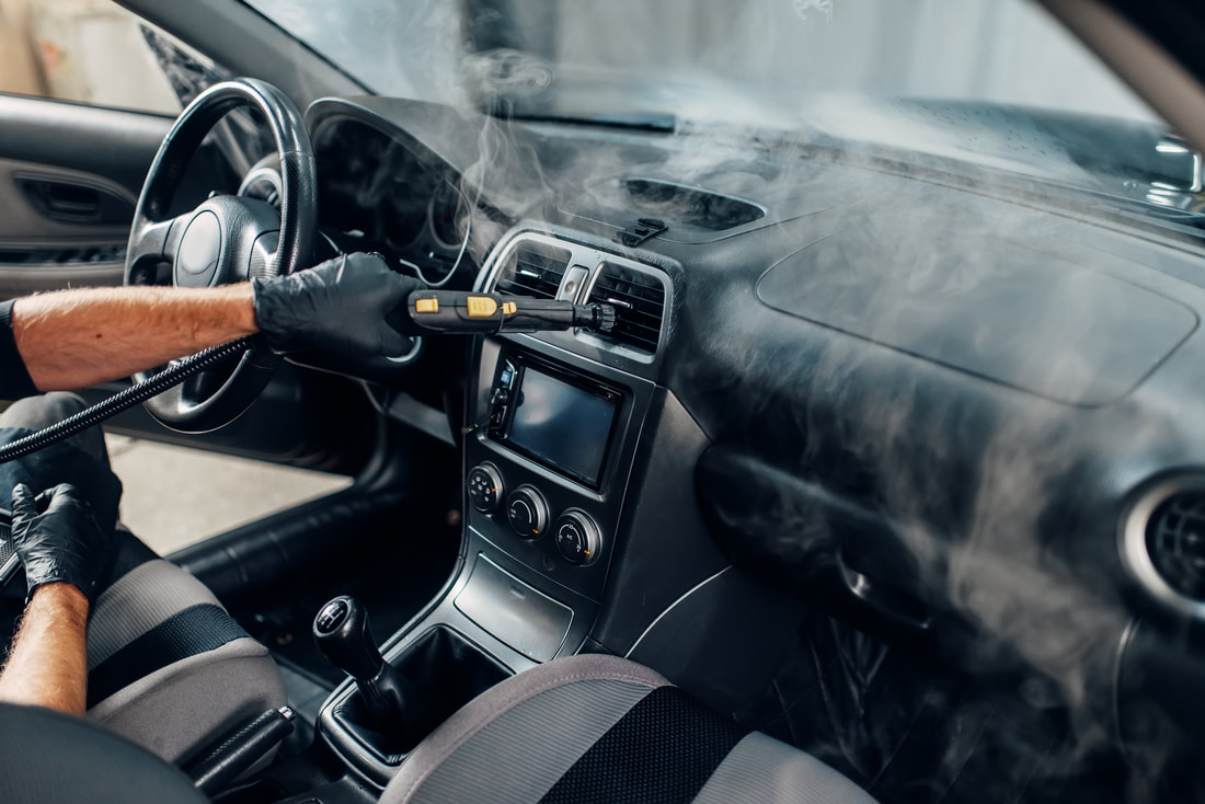 Steam cleaning a car dashboard and vents during an interior detailing service.